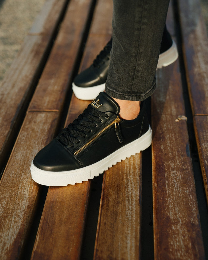 Martin Valen men's low-top black sneakers worn on feet, three-quarter view showing gold zipper, contrast laces and white sole